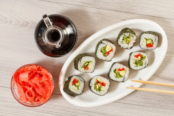 Rotoli di sushi con riso su piatto di ceramica, bacchette, bottiglia di vetro con salsa di soia e zenzero sottaceto in una ciotola — Foto Stock
