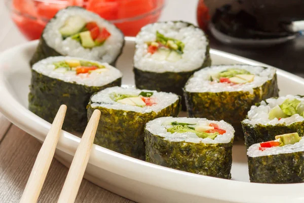 Rotoli di sushi con riso su piatto di ceramica, bacchette, bottiglia di vetro con salsa di soia e zenzero sottaceto in una ciotola . — Foto Stock