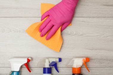 Ahşap arka planda deterjan şişeleri ile peçete tutan lastik eldiven el.