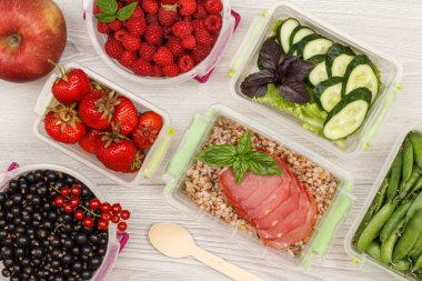 Haşlanmış karabuğday lapası ve et dilimleri, taze sebze ve çilek ile Elma ve plastik yemek hazırlama kapları.