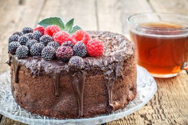 Çay bardağı ile cam tabak üzerinde siyah ve kırmızı ahududu ile dekore edilmiş ev yapımı çikolatalı kek