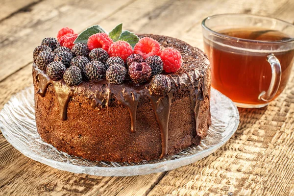 Çay bardağı ile cam tabak üzerinde siyah ve kırmızı ahududu ile dekore edilmiş ev yapımı çikolatalı kek.