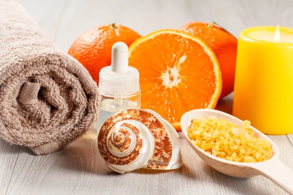 Cut orange with two whole oranges, towel, sea shell, bottle with aromatherapy oil, wooden spoon with yellow sea salt and burning candle
