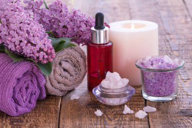 Deniz tuzu, yanan mum, aromatik yağ ile kırmızı şişe, leylak çiçekler ve ahşap tahtalar üzerinde havlu ile Kaseler.