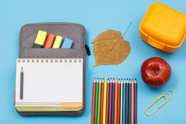 Renkli kalemler, elma, yemek kutusu, kuru yaprak, mavi arka plan çanta-kalem durumda açık egzersiz kitabı.