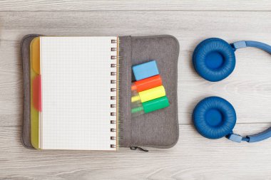 Renkli keçeli kalem ve marker ile çanta-kalem durumda açık egzersiz kitabı, gri ahşap panoları kulaklıklar.