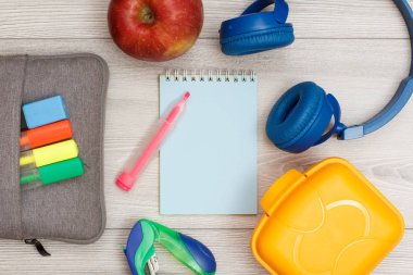 Renkli keçeli kalem ve marker, elma, dizüstü bilgisayar, kulaklık, zımba ve yemek kutusu ile çanta-kalem durumda.
