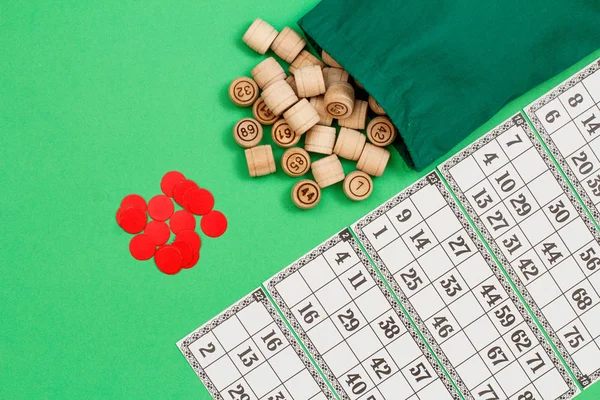 Barils de loto en bois avec sac, cartes à jouer et jetons rouges sur fond vert . — Photo
