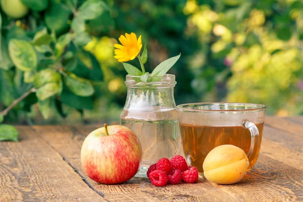 Olgun meyveler, cam şişede saplı calendula çiçeği ve bir fincan yeşil çay. — Stok fotoğraf