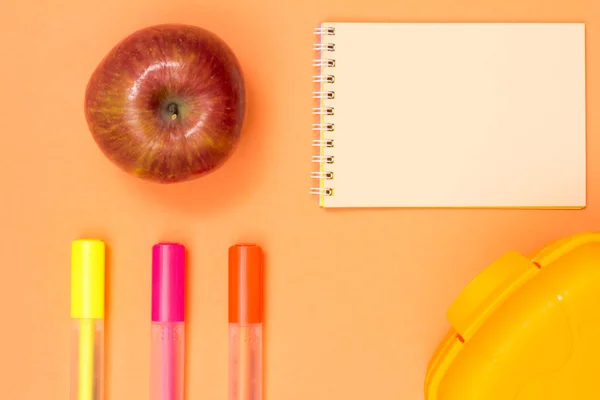 Maçã, caderno, canetas de feltro a cores e lancheira em fundo rosa — Fotografia de Stock