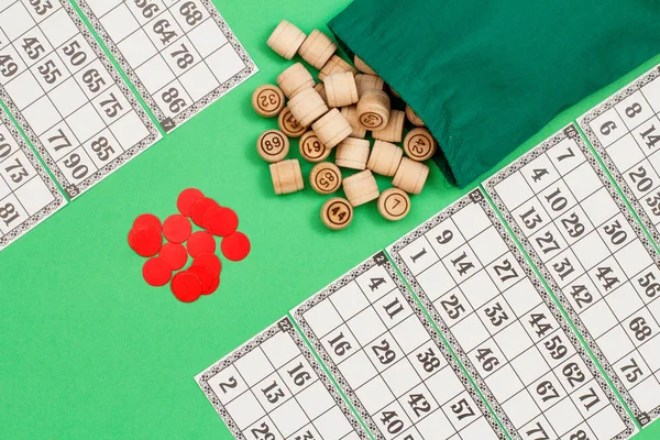 Barils de loto en bois avec sac, cartes à jouer et jetons rouges sur fond vert . — Photo