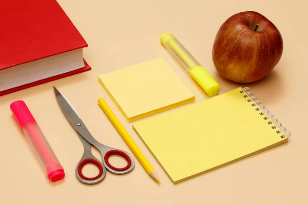 Livre, ciseaux, crayon, carnet, papier à lettres, feutre et pomme sur fond beige — Photo