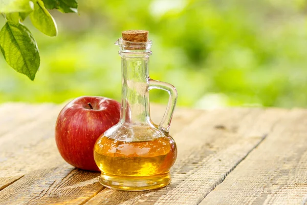 Apfelessig in Glasflasche und frischer roter Apfel auf Holzschwein — Stockfoto