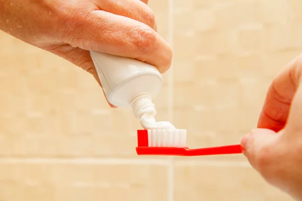 Red toothbrush and tube of toothpaste in female hands. — Stock Photo, Image