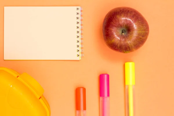 Maçã, caderno, canetas de feltro a cores e lancheira em fundo rosa — Fotografia de Stock