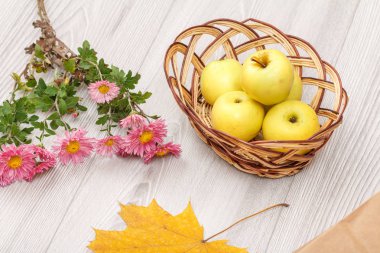 Ahşap masa üzerinde hasır sepeti ve çiçekler olgun elma.