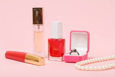 Ruj, parfüm, oje ve pembe arka plan üzerinde yüzük ile kutu.