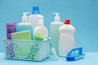 Sepette bulaşık sıvısı şişeleri, mavi arka planda sünger ler ve fırçalar.