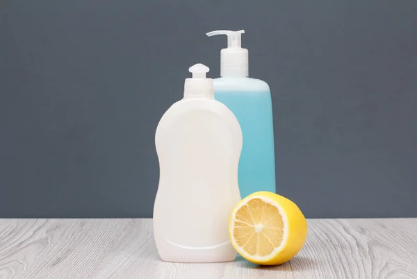 Bottles of dishwashing liquid and lemon on gray background.