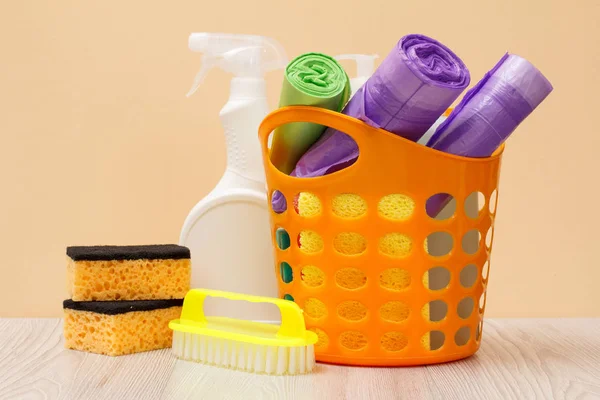 Botella de líquido lavavajillas, cesta con bolsas de basura y esponjas en escritorio de madera . — Foto de Stock