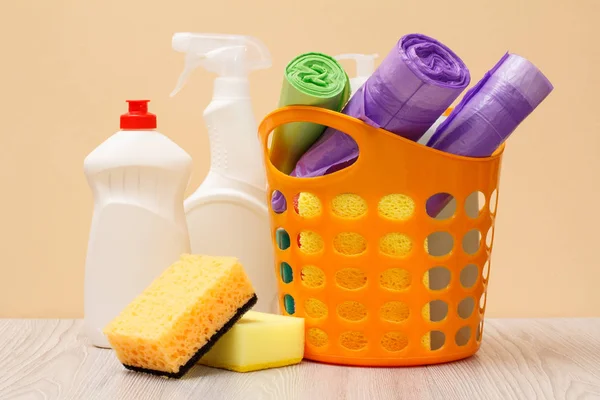 Botellas de líquido lavavajillas, cesta con bolsas de basura y esponjas en escritorio de madera . — Foto de Stock