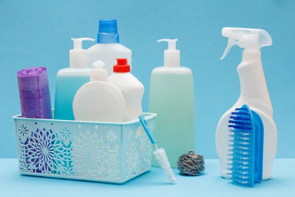 Botellas de líquido lavavajillas en cesta, esponjas y cepillos sobre fondo azul . — Foto de Stock