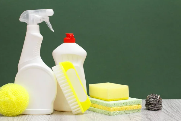 Bottles of dishwashing liquid, brush and sponges on green background.