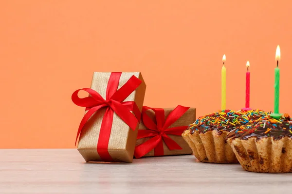 Tasty birthday muffin with burning festive candle and gift boxes.