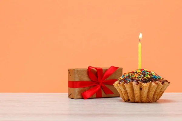 Sabroso panecillo de cumpleaños con vela festiva ardiente y una caja de regalo . — Foto de Stock