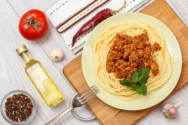 Plate with spaghetti bolognese and vegetables, spices for cooking on wooden board.