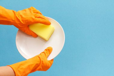 Mavi arka plan üzerinde sünger ve plaka ile koruyucu eldiven kadın elleri.