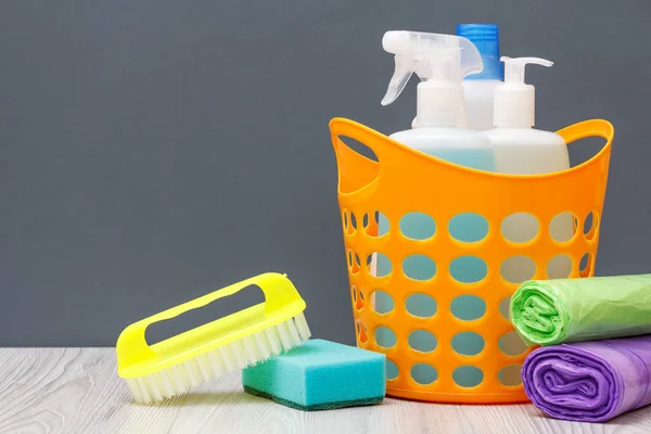 Botellas de líquido lavavajillas, cepillo en una cesta y esponja, bolsas de basura sobre fondo gris . — Foto de Stock