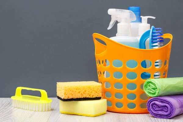 Botellas de líquido lavavajillas, cepillo en una cesta y esponjas, bolsas de basura sobre fondo gris . — Foto de Stock