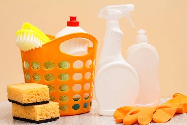 Flaskor med diskmedel, gummi handske, korg och svamp på beige bakgrund. — Stockfoto