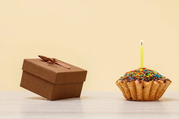 Sabroso panecillo de cumpleaños con vela festiva ardiente y caja de regalo sobre fondo beige . — Foto de Stock