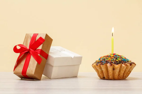 Cajas de regalo y magdalena de cumpleaños con vela festiva ardiente sobre fondo beige . — Foto de Stock