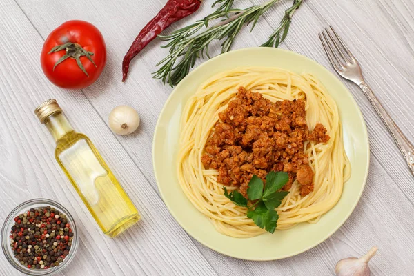 Placa con espaguetis boloñesa y verduras, especias para cocinar sobre tabla de madera . —  Fotos de Stock