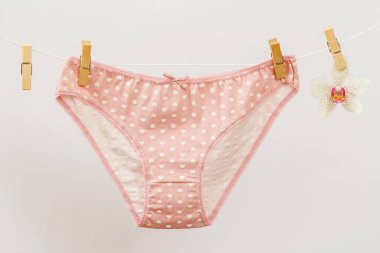 Çamaşır ipinde yeni pembe külotlar, mandallı ve beyaz arka planda orkide çiçekli. Kadın iç çamaşırı.