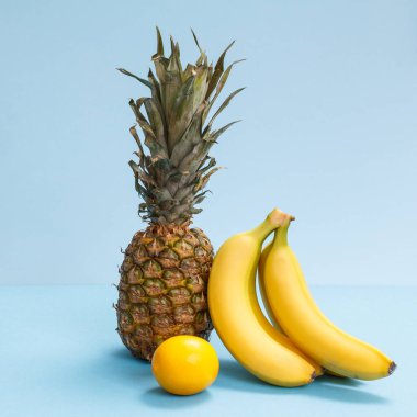Tropikal meyveli doğal bileşim. Taze ananas, muz ve mavi arka planda bir limon..
