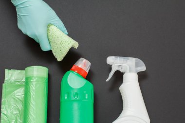 Siyah arka planda sünger ve temizlik seti olan koruyucu eldivenli bir kadın eli. Üst görünüm.