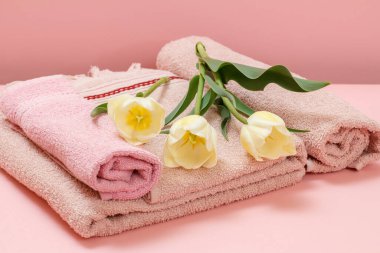 Pembe arka planda sarı laleli yumuşak havlu yığını..