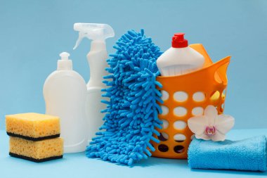 Plastik sepet, bulaşık deterjanı şişeleri, mavi arka planda bez ve süngerler. Yıkama ve temizleme seti.