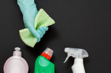 Koruyucu eldivenli bir kadın eli, siyah arka planda bir bez, çamaşır ve temizlik seti. Üst görünüm.