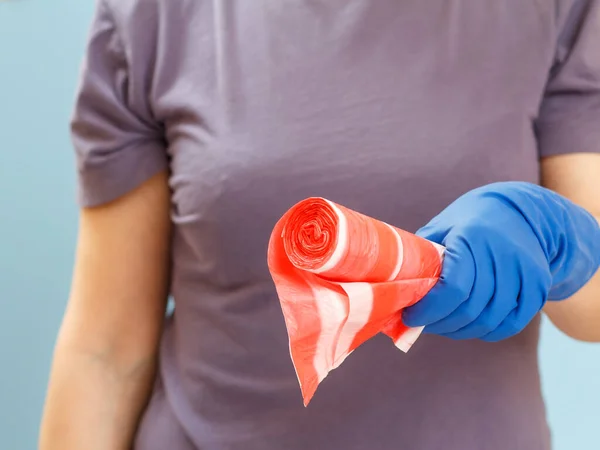 Woman in a t-shirt holding garbage bags on the blue background. Shallow depth of field. Focus on bags. Washing and cleaning concept.