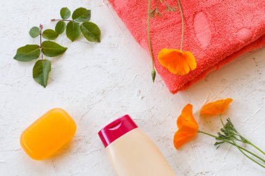 Beyaz arka planda bir şişe şampuan, havlu, sabun ve Escholzia California çiçeği. Kadın kozmetik ve aksesuarları. Üst görünüm.