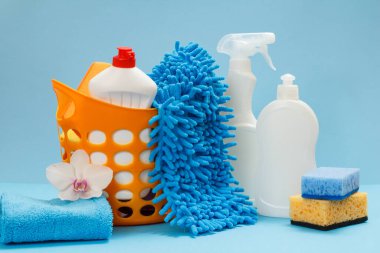 Plastik sepet, bulaşık deterjanı şişeleri, mavi arka planda bez ve süngerler. Yıkama ve temizleme seti.