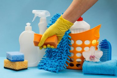 Sarı nitril eldivenli bir kadının eli. Mavi arka planda yıkama ve temizleme seti olan bir sünger tutuyor..