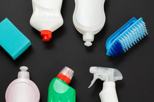 Plastic bottles of washing liquid, a brush and a sponge on the black background. Top view. Washing and cleaning set.