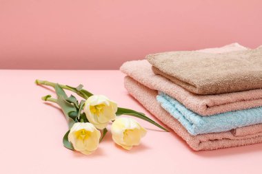 Pembe arka planda sarı laleli yumuşak havlu yığını..
