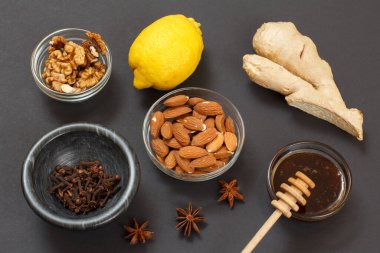 Soğuk algınlığı için sağlıklı besinler ve siyah arka planda limon, zencefil, bal ve fındıklı grip ilacı. Üst Manzara. Bağışıklık sistemini güçlendiren gıdalar.